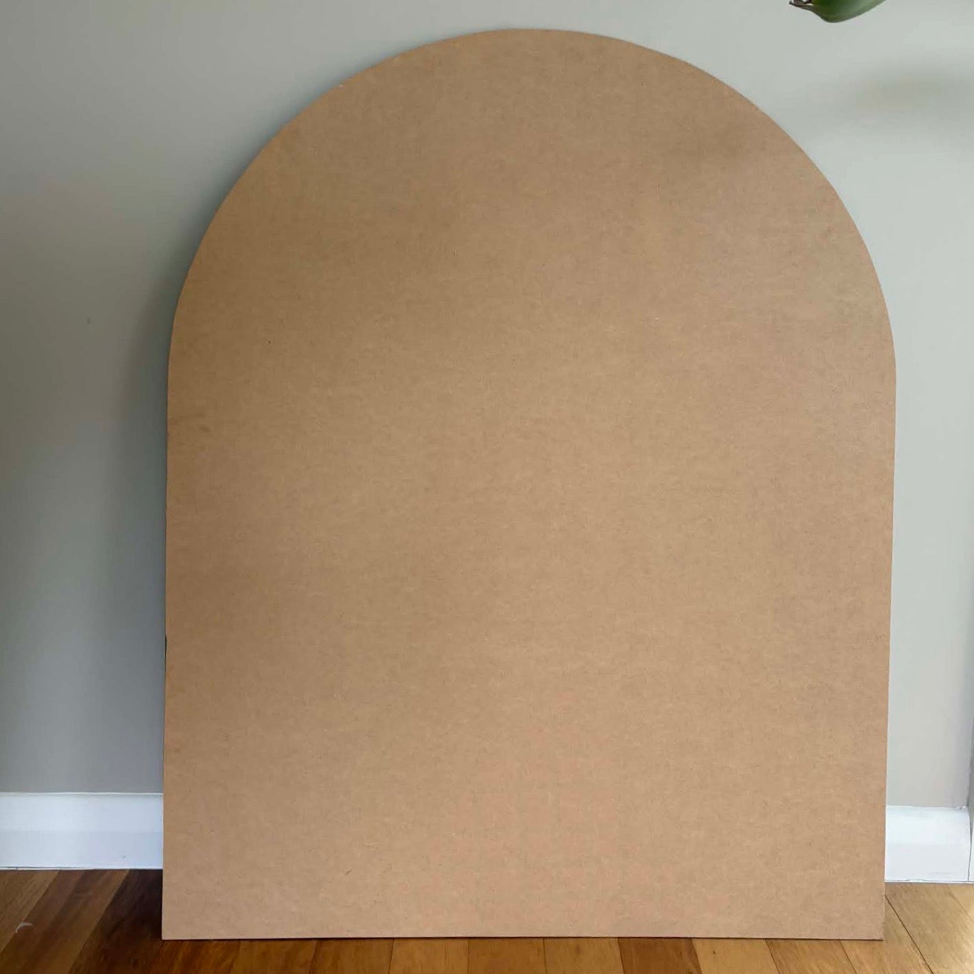 Arch-shaped MDF board piece against a neutral wall. MDF baxkboard for the MAgnetic Playwall by Peasy Play. 