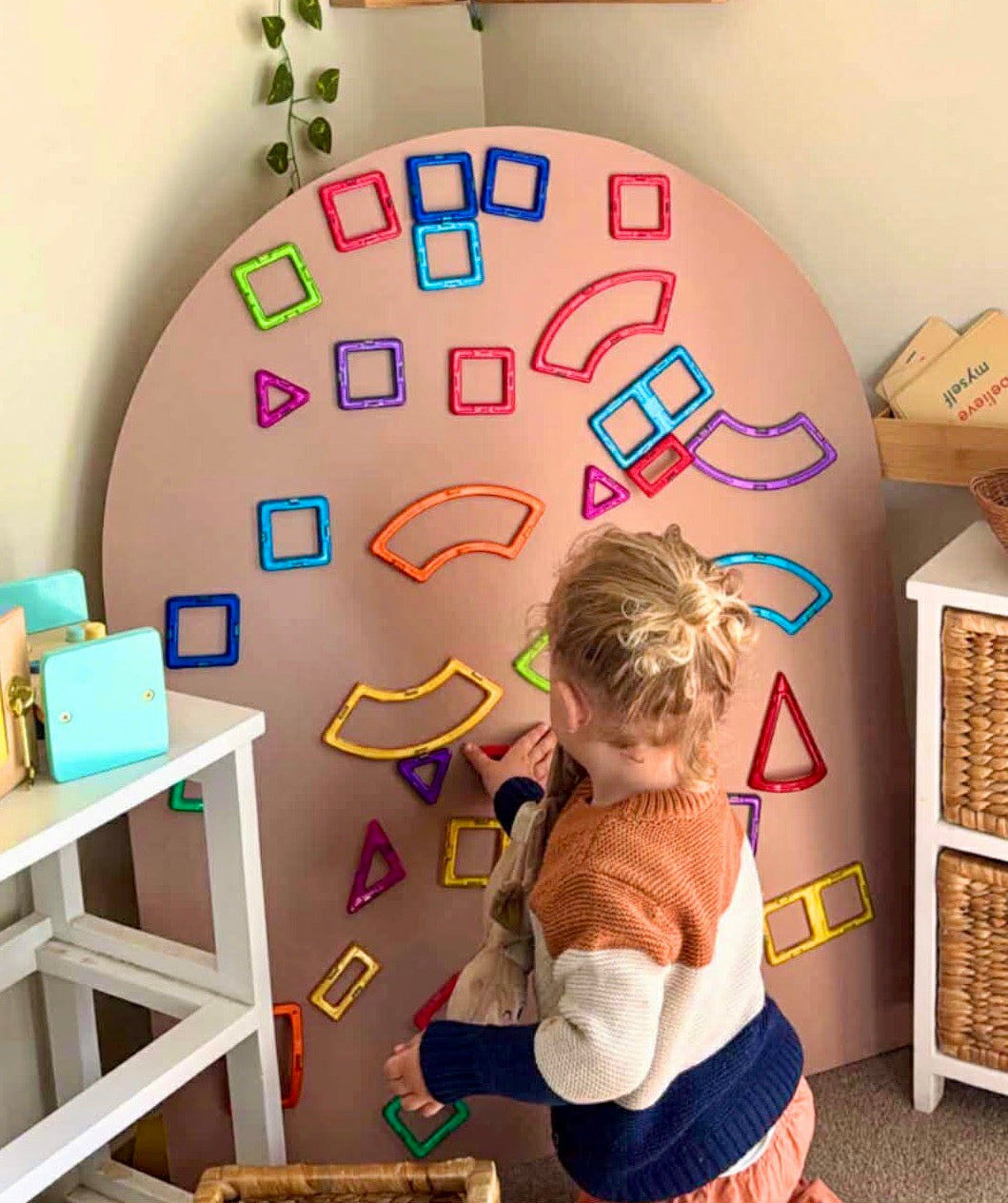 Child playing with colorful magnetic tiles and shapes on the rosewood magnetic playwall on MDF board in a playroom.