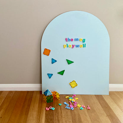 Children's magnetic play wall toy on MDF board with magnetic tiles, shapes and letters on a wooden floor.